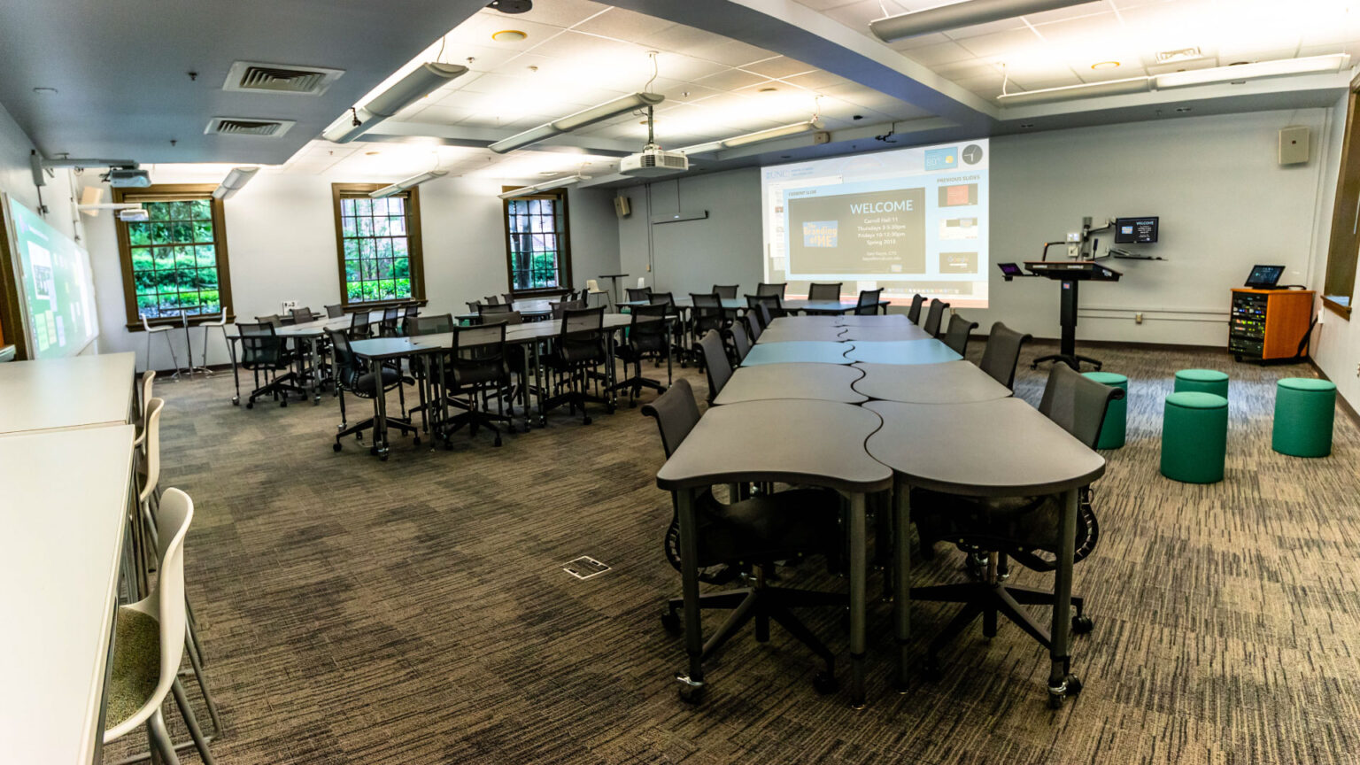 Interior of a classroom with projector, lectern, AV stand, and many modular student desks. 