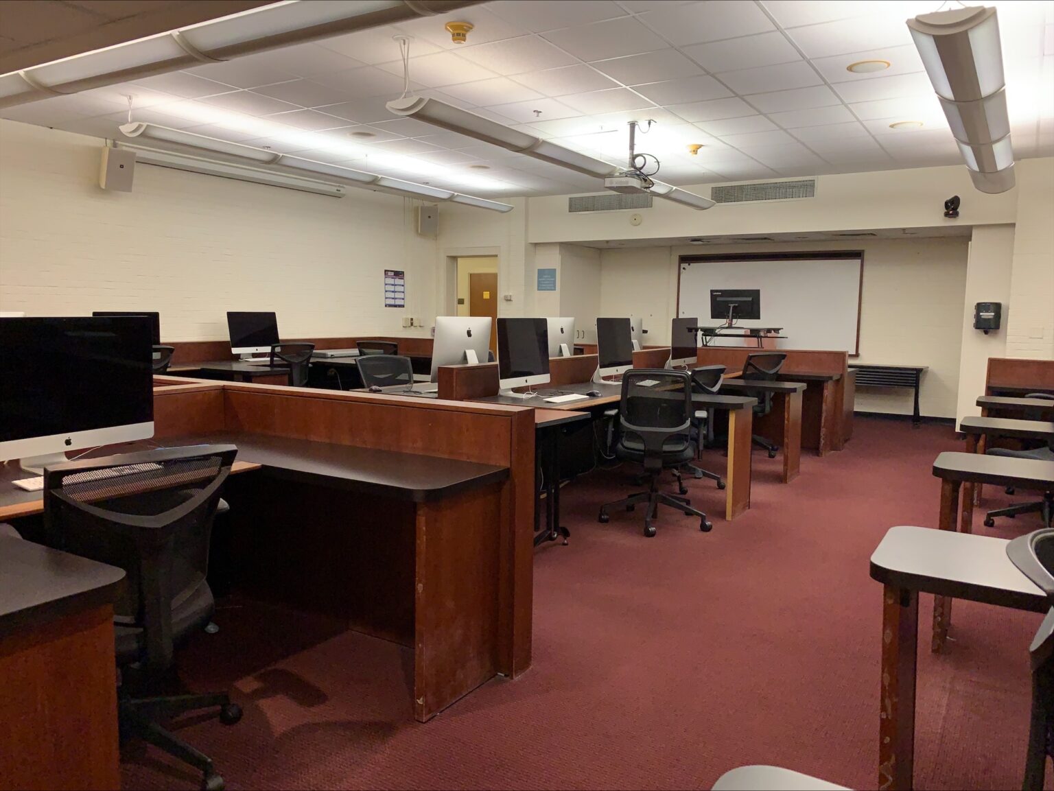 Interior of a classroom with wooden desks and Mac monitors. 