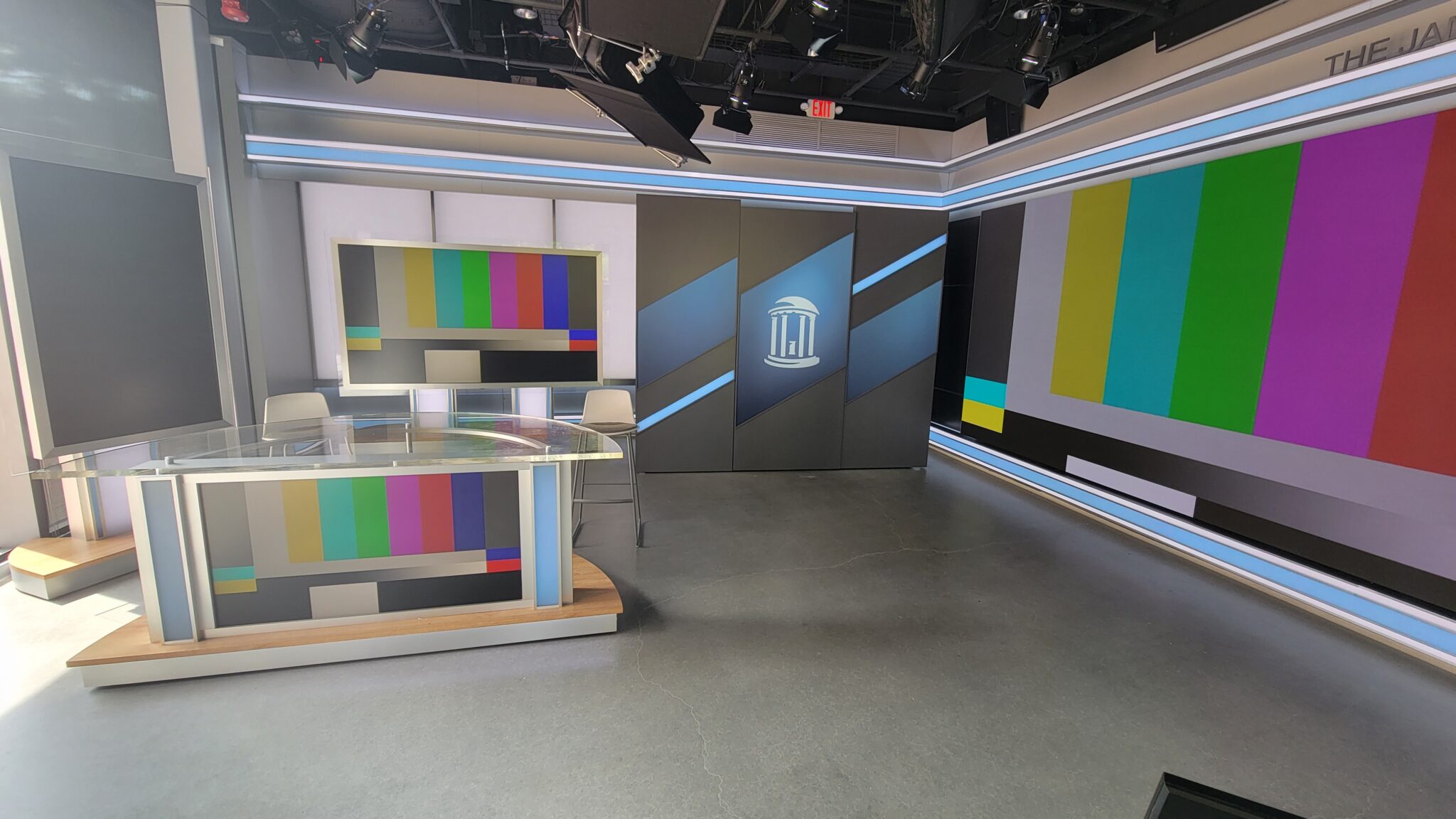 Room with a news desk and multiple screens for media production.
