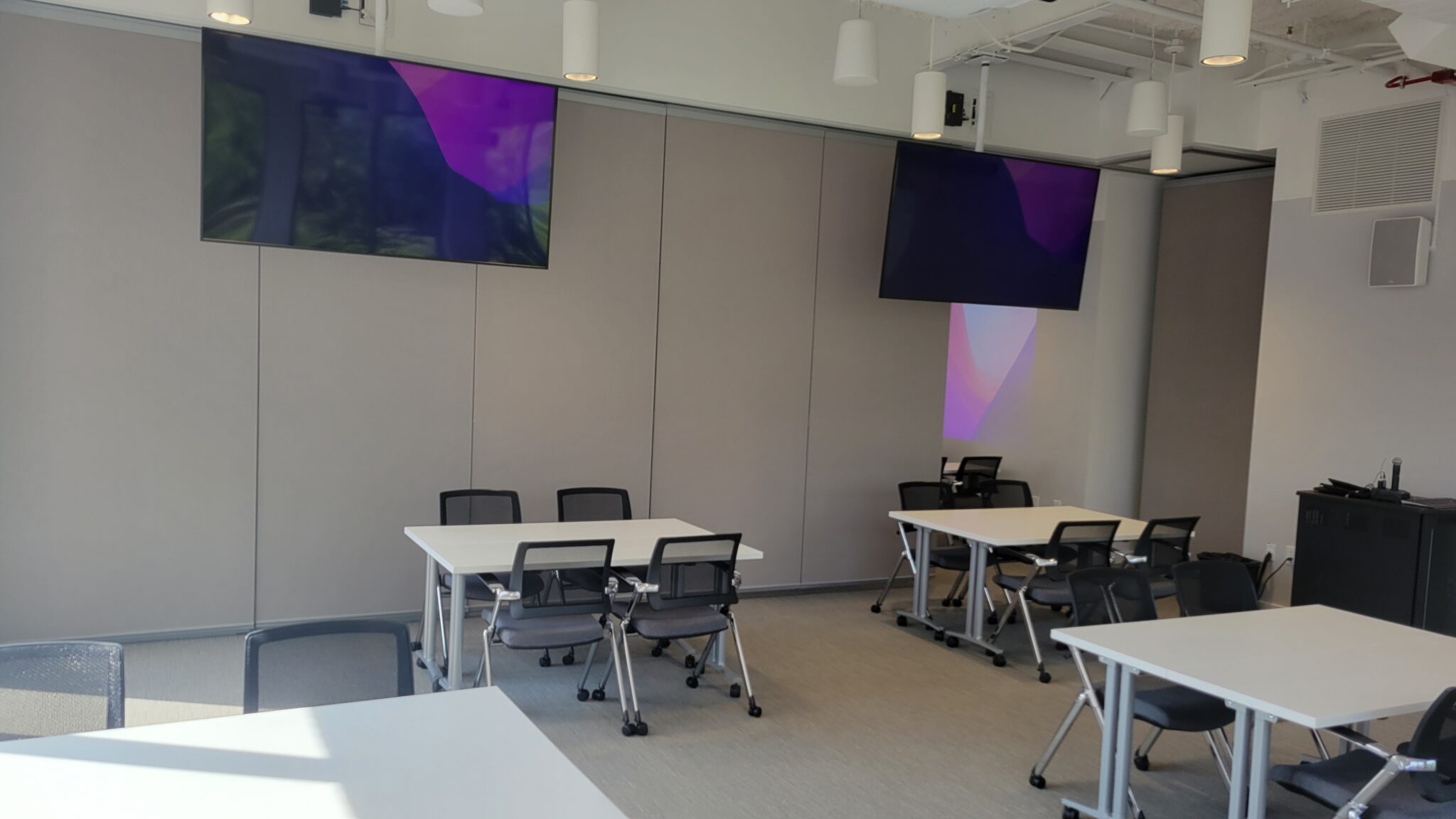 Classroom with mounted monitors and small groups of desks.